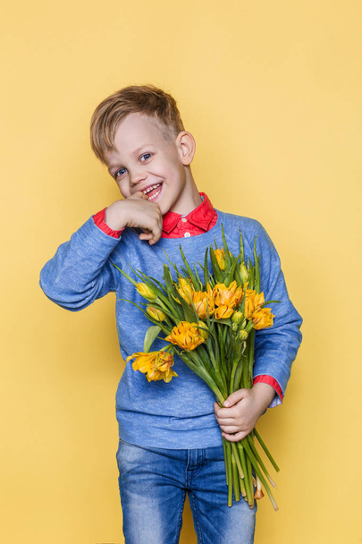 Little beautiful child with a bouquet of tulips. Son gives mom flowers on Women's Day, Mother's Day. Birthday. Valentine's day. Spring. Studio portrait over yellow background - Photo, image