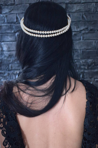 оголена спина молодої дівчини з чорним волоссям і перлами
 - Фото, зображення