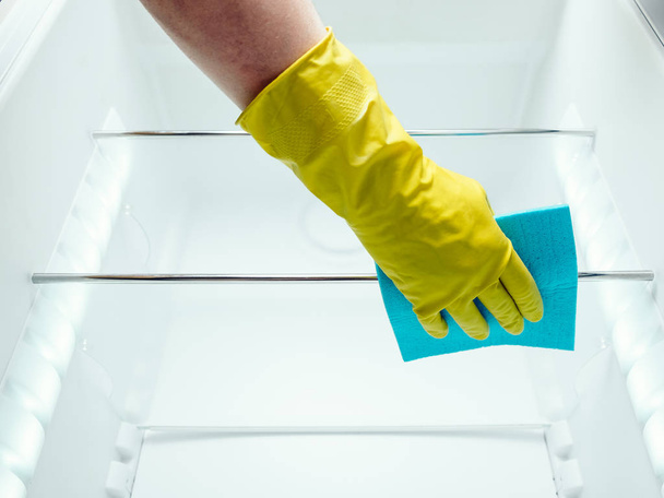 Man's hand cleaning white fridge with blue rag - Foto, afbeelding