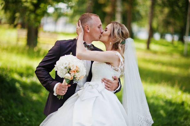 Fashionable kissing wedding couple hugging at green park on sunn - Photo, image