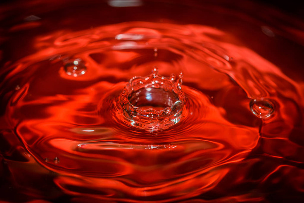 Water drop an waves with red background and reflection - Photo, Image