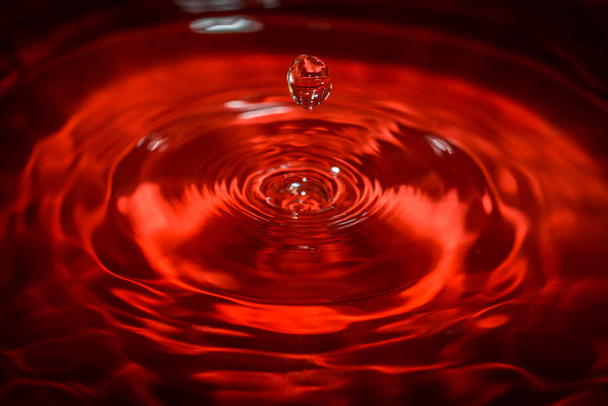 Water drop an waves with red background and reflection - Photo, Image