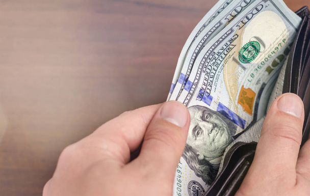 Крупный план мужской руки, берущей банкноты по сто долларов из бумажника, деревянного фона, денег и финансовой концепции
 - Фото, изображение