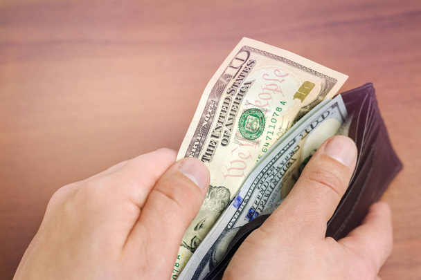 Közelkép a férfi kézről, amint 100 dolláros bankjegyeket vesz ki pénztárcából, fából, pénzből és pénzügyi koncepcióból - Fotó, kép
