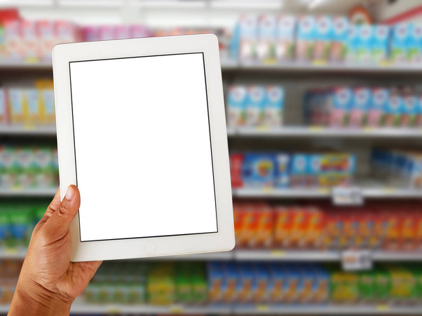 asian left hand holding blank tablet screen on blurred various brand of milk and dairy products in packaging for sale on supermarket stand or shelf  - Photo, Image