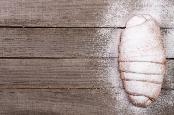 un croissant saupoudré de sucre en poudre sur un vieux fond en bois avec de l'espace pour copier votre texte. Vue du dessus
 - Photo, image