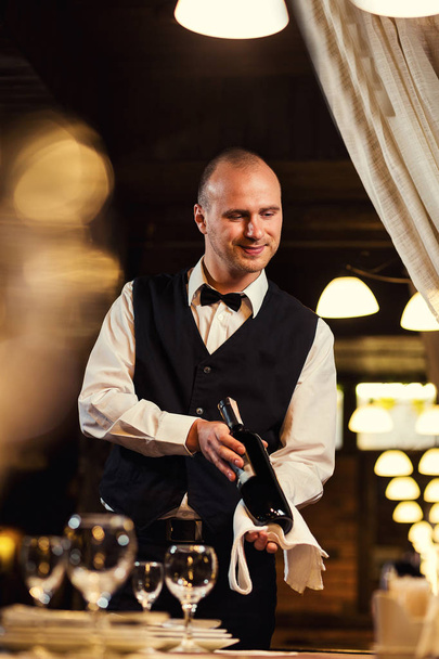 The waiter offers visitors wine,Waiter in uniform waiting an order,Waiter with a white towel on his hand,Confident waiter,A pub.Restaurant.Classic.Evening.European restaurant - Photo, Image