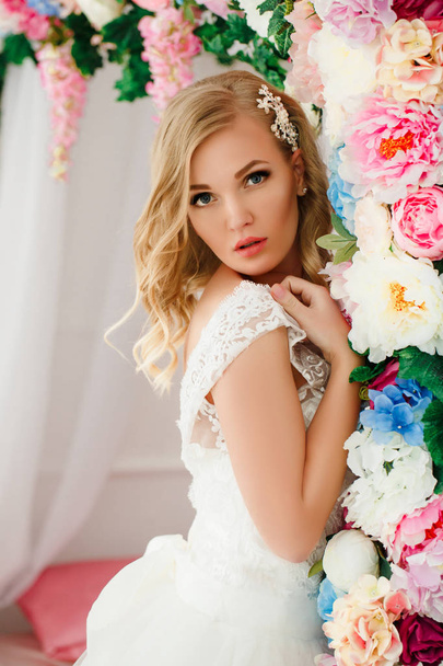 Young woman wearing wedding dress posing in room decorated with flowers - Foto, Bild
