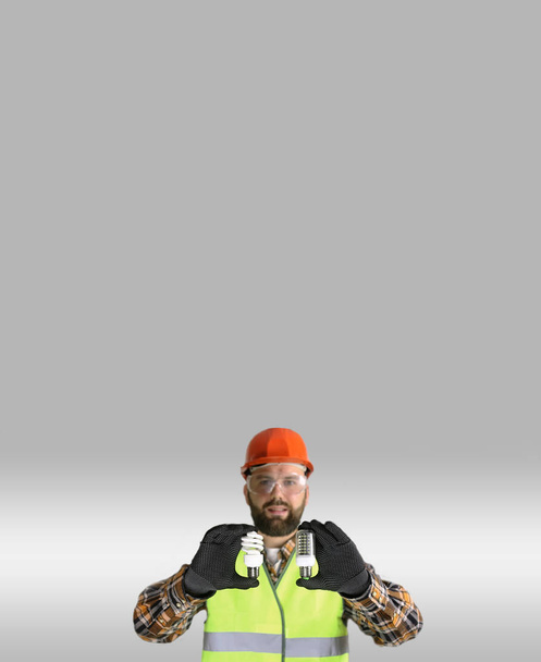 Arbeiter mit Helm und Schutzkleidung mit Glühbirne in der Hand - Foto, Bild