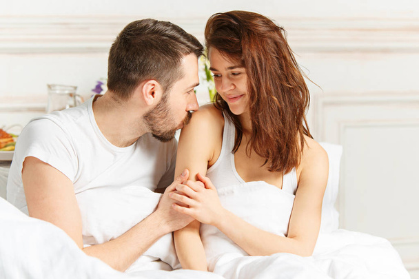 Young adult heterosexual couple lying on bed in bedroom - Фото, изображение