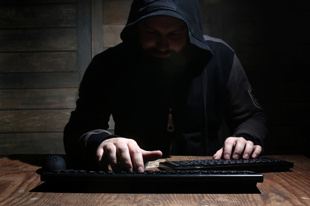 hacker no capuz preto em uma sala com paredes de madeira
 - Foto, Imagem