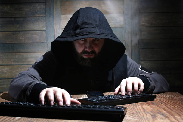 hacker en la capucha negra en una habitación con paredes de madera
 - Foto, Imagen