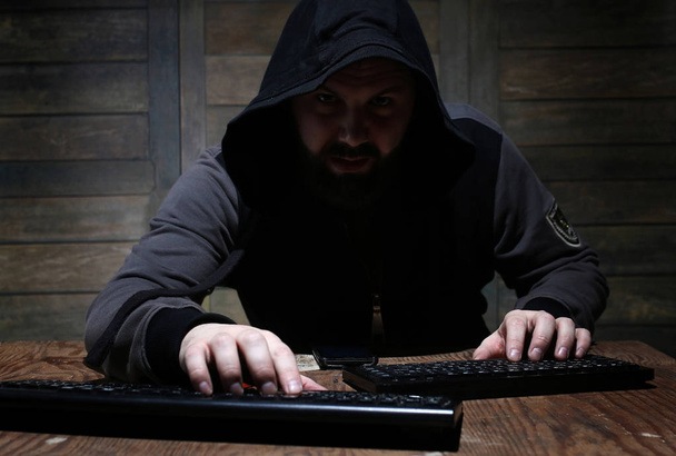 hacker in de zwarte kap in een kamer met houten muren - Foto, afbeelding