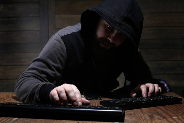 Hacker in der schwarzen Haube in einem Raum mit Holzwänden - Foto, Bild