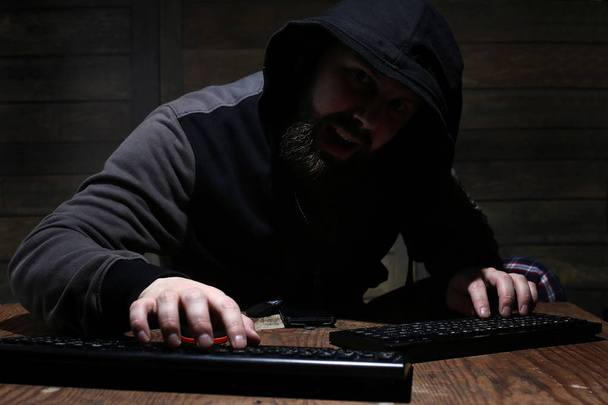 χάκερ στην μαύρη κουκούλα σε ένα δωμάτιο με ξύλινα τείχη - Φωτογραφία, εικόνα