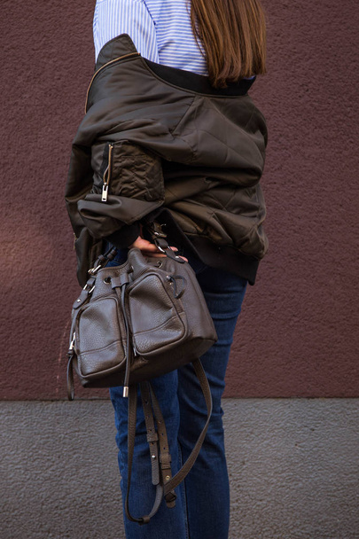 идеальный весенний наряд. Европейский блогер моды одет в модную полосатую блузку с передним узлом и куртку подрывника. Держать стильную сумку
. - Фото, изображение