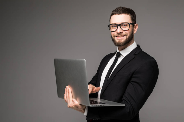 Beau homme d'affaires en lunettes et costume tenant ordinateur portable dans les mains et en écrivant quelque chose vue de côté isolé fond gris
 - Photo, image