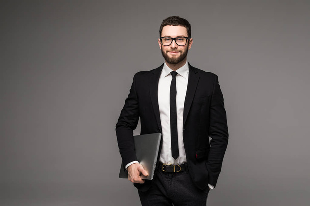 Hombre de negocios guapo en gafas y traje que sostiene el ordenador portátil en las manos vista lateral aislado fondo gris
 - Foto, imagen