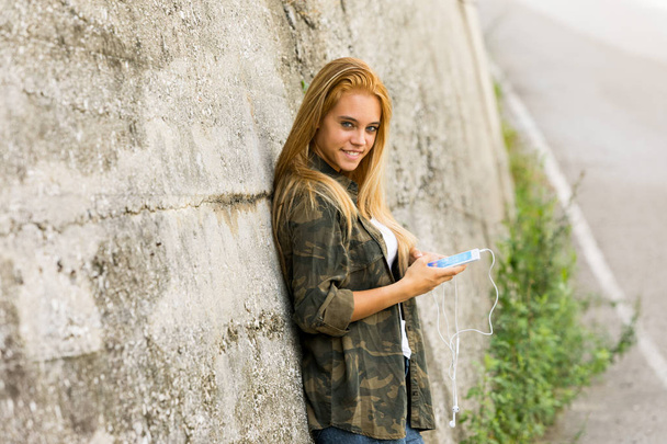 menina ao ar livre com um celular olhando para camer
 - Foto, Imagem