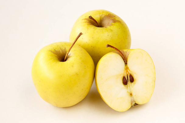 halb geschnittene und ganze goldene köstliche Äpfel auf hellbeigem Hintergrund - Foto, Bild