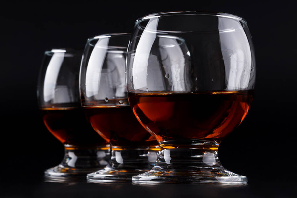 Tre bicchieri con cognac di fila su fondo nero
 - Foto, immagini