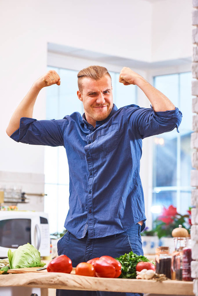 Uśmiechnięty mężczyzna z rąk się pokazując mięśnie i moc warzyw zdrowe jedzenie - Zdjęcie, obraz