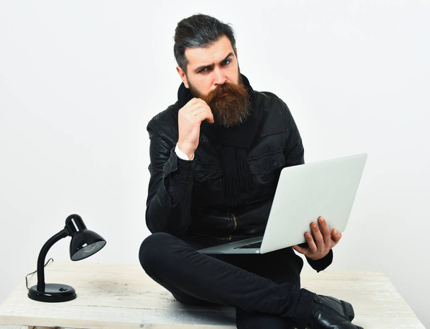 Bearded brutal caucasian hipster sitting on table with laptop - Фото, зображення
