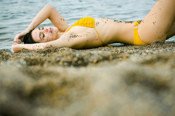 Pretty girl in yellow swimsuit sleeping on sea beach - Foto, Imagen