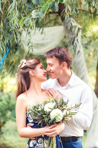 Happy young newlywed couple touching noses in park. Holding a bouquet. Romantic  - Photo, Image