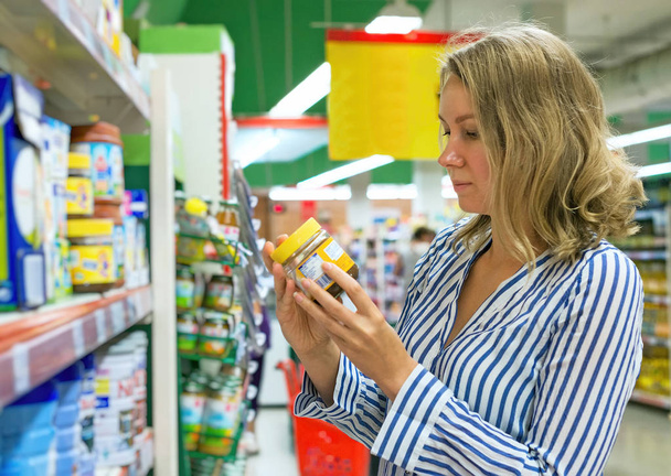 Молода жінка вибирає дитяче харчування в супермаркеті
. - Фото, зображення