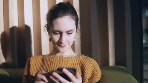 Portrait of young beautiful woman sitting in sofa and using smartphone. Girl chatting with friends in the morning. - Materiaali, video