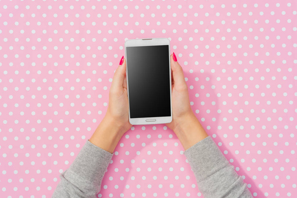 Female hands using white smart phone over pink dotted background - Fotografie, Obrázek