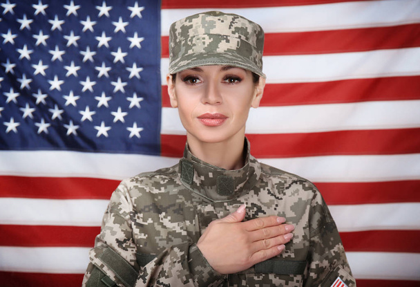 Female soldier holding hand on heart, with USA flag on background - 写真・画像