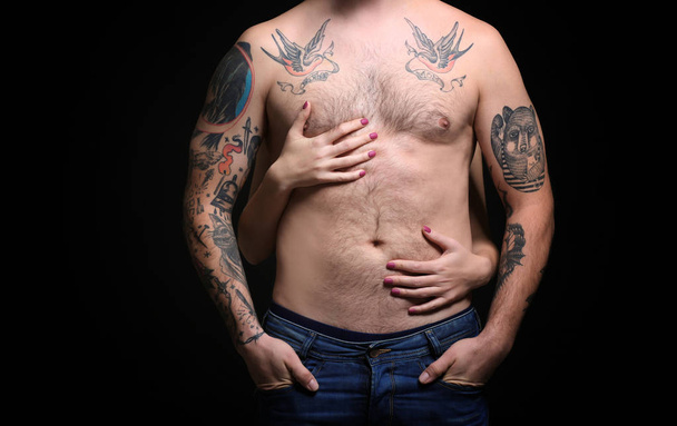 Tattooed man with a woman hands on body, black background - 写真・画像