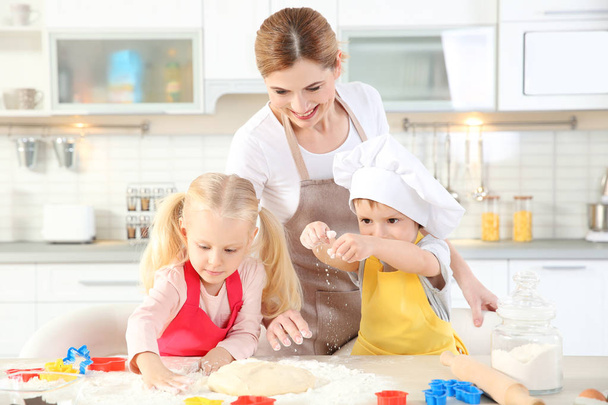 Young mother with kids making biscuits on table - Foto, imagen