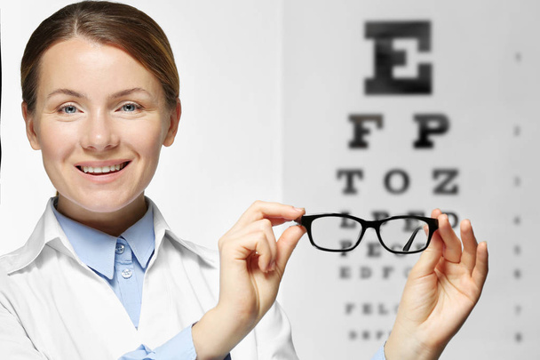 Young woman holding spectacles on eyesight test chart background - Foto, afbeelding