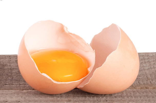 Uovo rotto con tuorlo e guscio d'uovo su un tavolo di legno con sfondo bianco
 - Foto, immagini