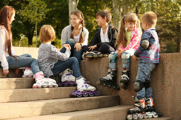 Cheerful friends in roller skates sitting on border in park - Фото, изображение
