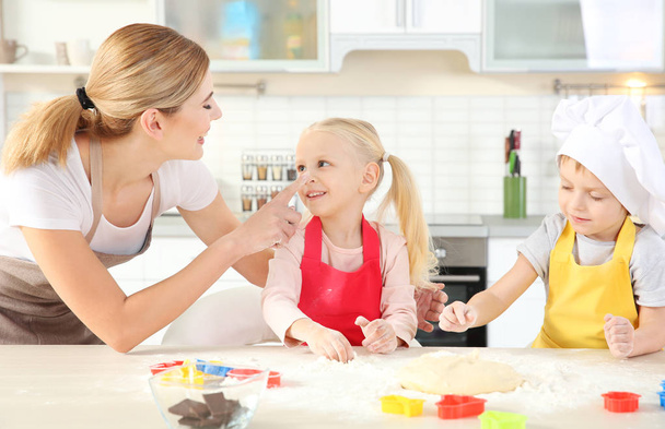 Young mother with kids making biscuits on table - Photo, image