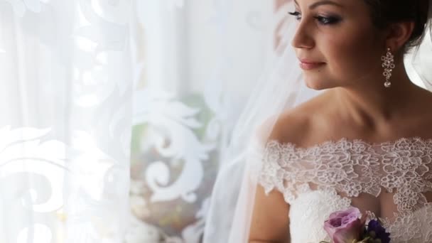 Mooie bruid in luxe trouwjurk op zoek door het raam voordat de ceremonie van het huwelijk. Vrouw bedrijf bloemen - Video