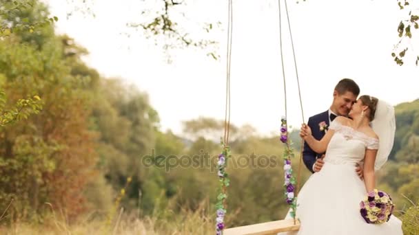 Bride and groom standing near the swing in the summer park. Hugging and kissing. - Footage, Video