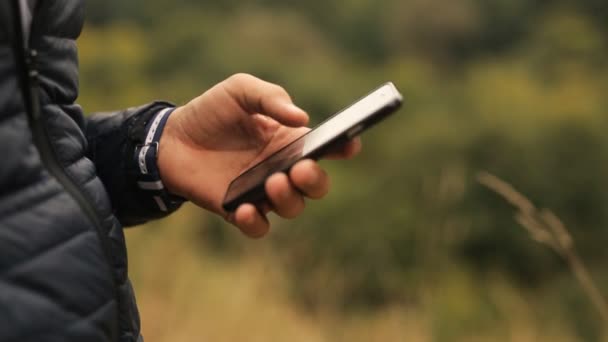 Az ember használ smartphone a parkban. Kéz black okostelefon, a park, szabadtéri közelről - Felvétel, videó