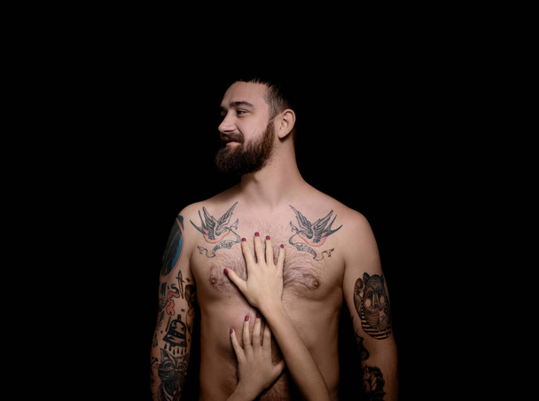 Tattooed man with a woman hands on body, black background - Foto, Imagen