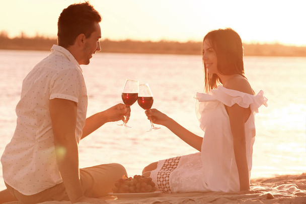 Young couple with wine having romantic date on sunset beach - Фото, изображение