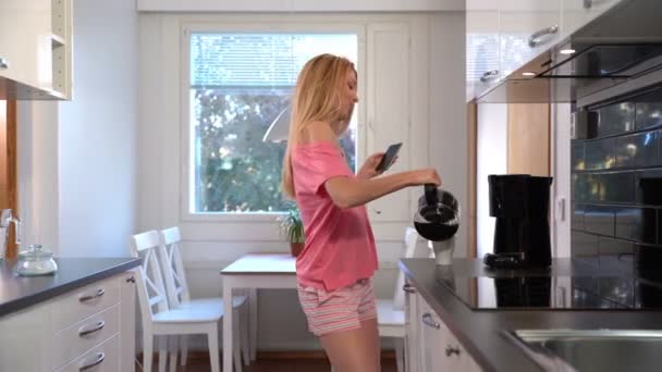 A happy woman in pajamas, dancing in the kitchen, coffee, headphones, smartphone. Dolly. - Video, Çekim