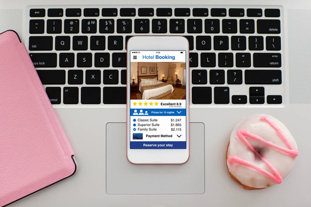 witte telefoon met app hotel reserveringsscherm op laptop toetsenbord - Foto, afbeelding
