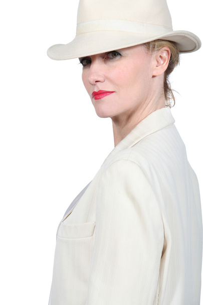 Foto de perfil de una mujer rubia que usa una suite de color crema con sombrero a juego
 - Foto, imagen