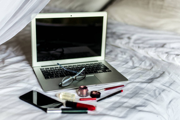 Espaço de trabalho nômade digital na cama branca com laptop, telefone e óculos
.  - Foto, Imagem