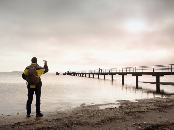 Wanderer mit Rucksack allein am Sandstrand, Sonnenaufgang über der Seebrücke. - Foto, Bild