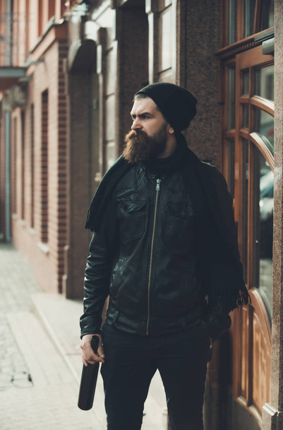 serious bearded man hipster with wine bottle in leather jacket - Foto, afbeelding